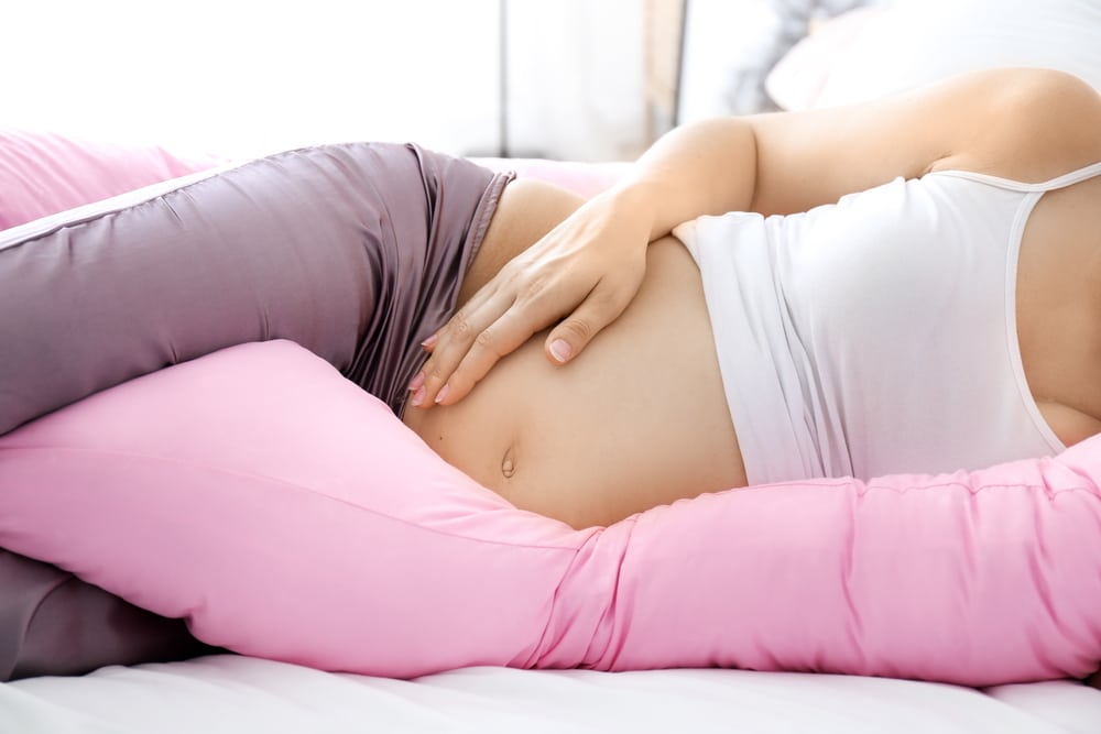 A pregnant woman sleeps on a pink-colored cushion